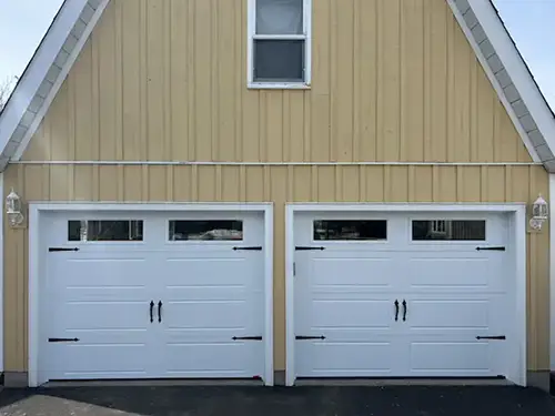 A yellow A-frame garage with white siding features two closed, white double garage doors. Each door has black handles and top windows.