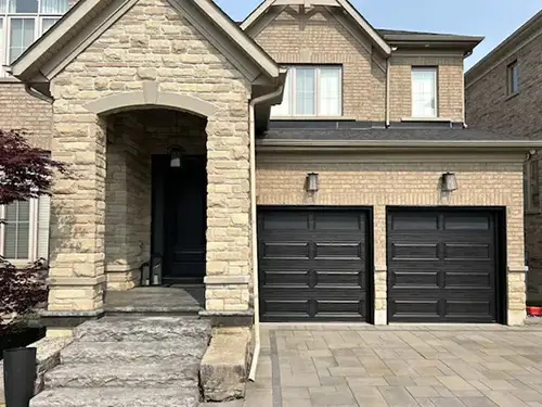 Stone house with a covered porch, dark garage doors, and a paved driveway.