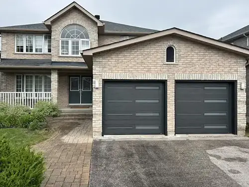 Two-story brick house with an arched window above and twin black garage doors.