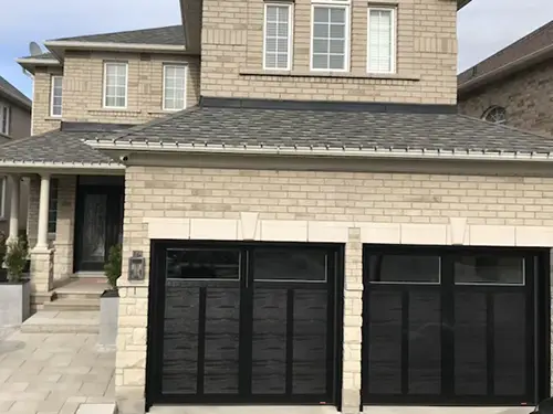 Two-story house with light brick facade, featuring two large black garage doors.