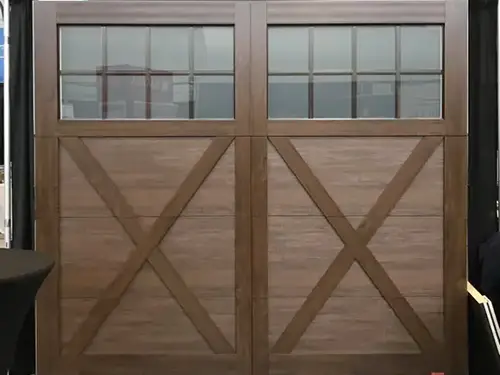 Wooden double garage doors with large X-patterns and rectangular glass panes on top.
