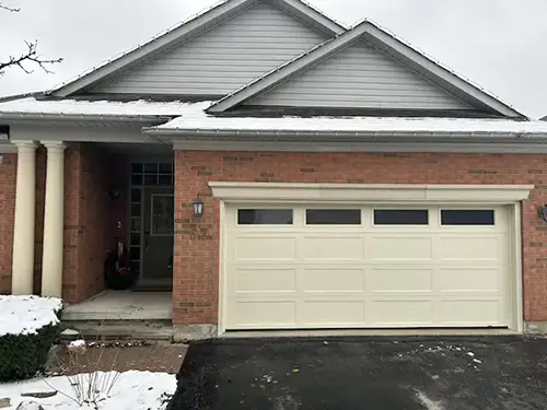 A snow-dusted brick house with a gray roof and beige garage door.