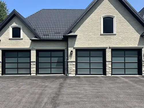 A modern house with four full-glass garage doors, light brick exterior, and dark roof under a clear blue sky, conveying a sleek, contemporary feel.